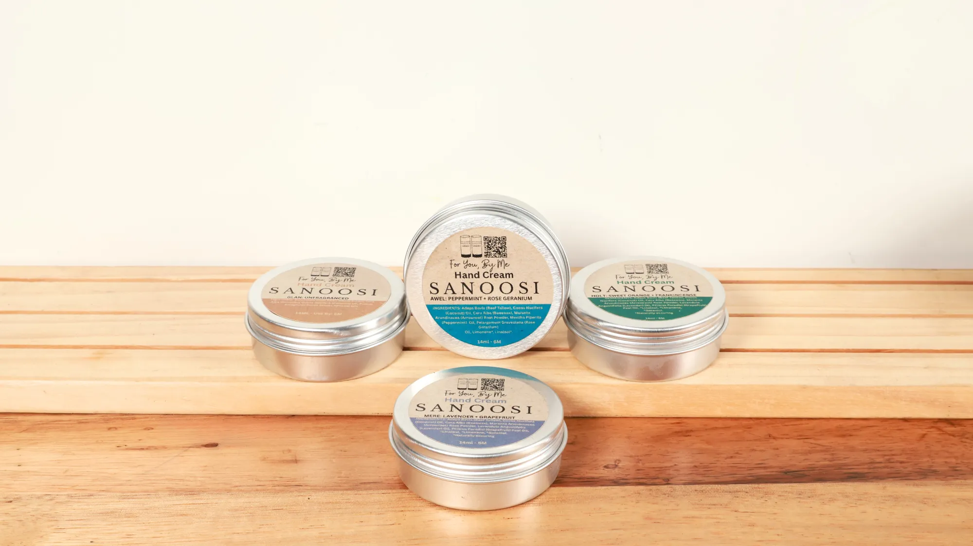 SANOOSI hand cream tins in each scent, stacked on a wooden shelf