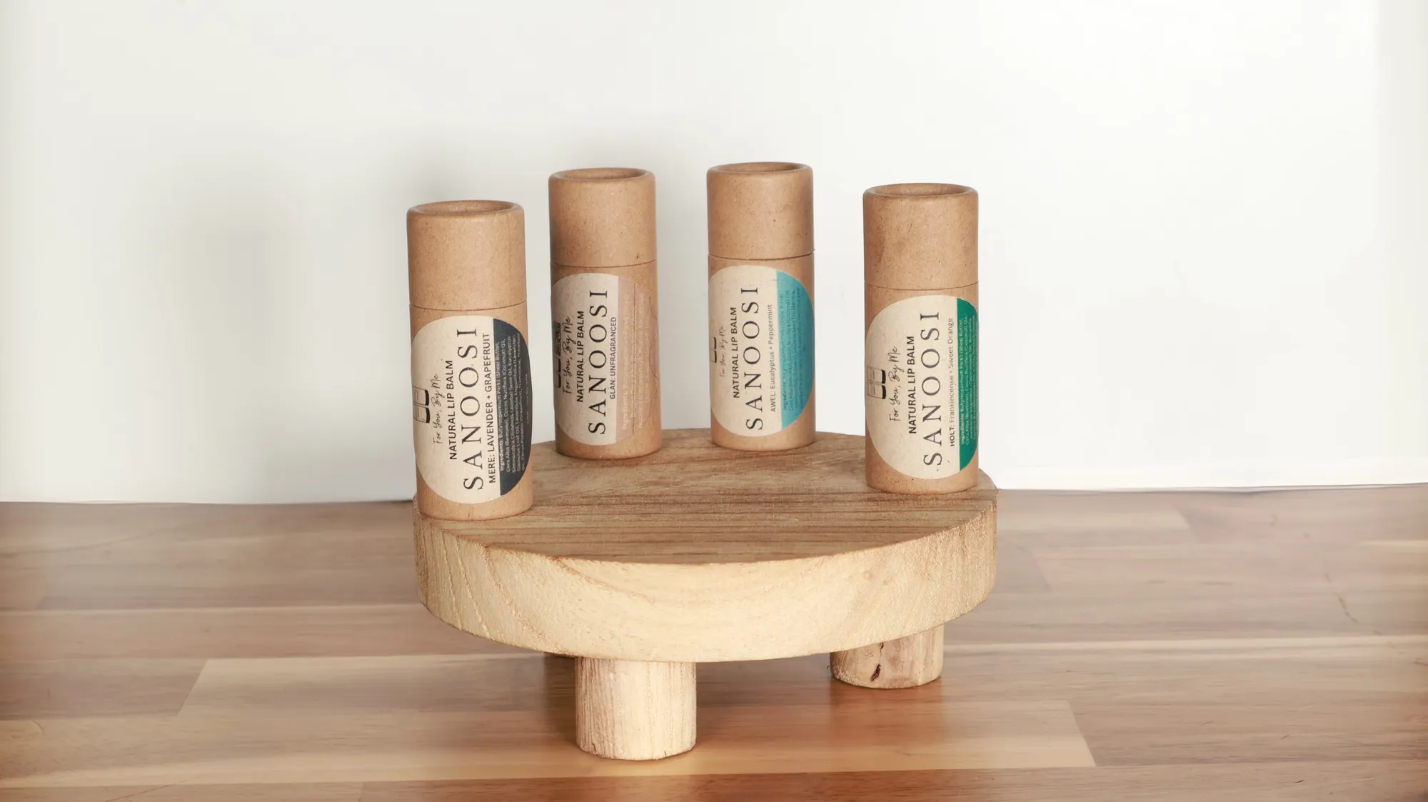 Four SANOOSI natural lip balms on a wooden stand